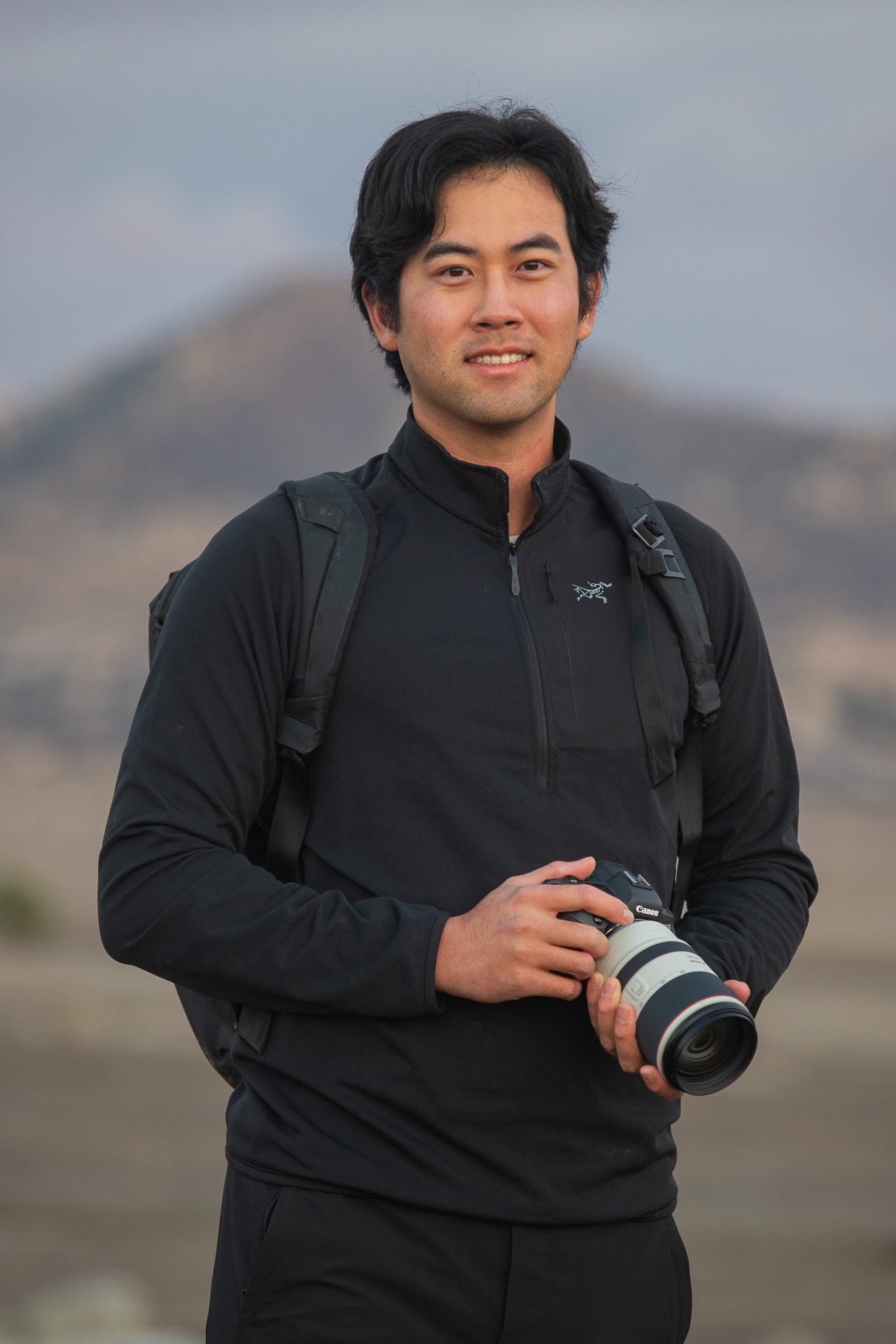 Dr. Matthew Im standing with his camera in the hills at dusk